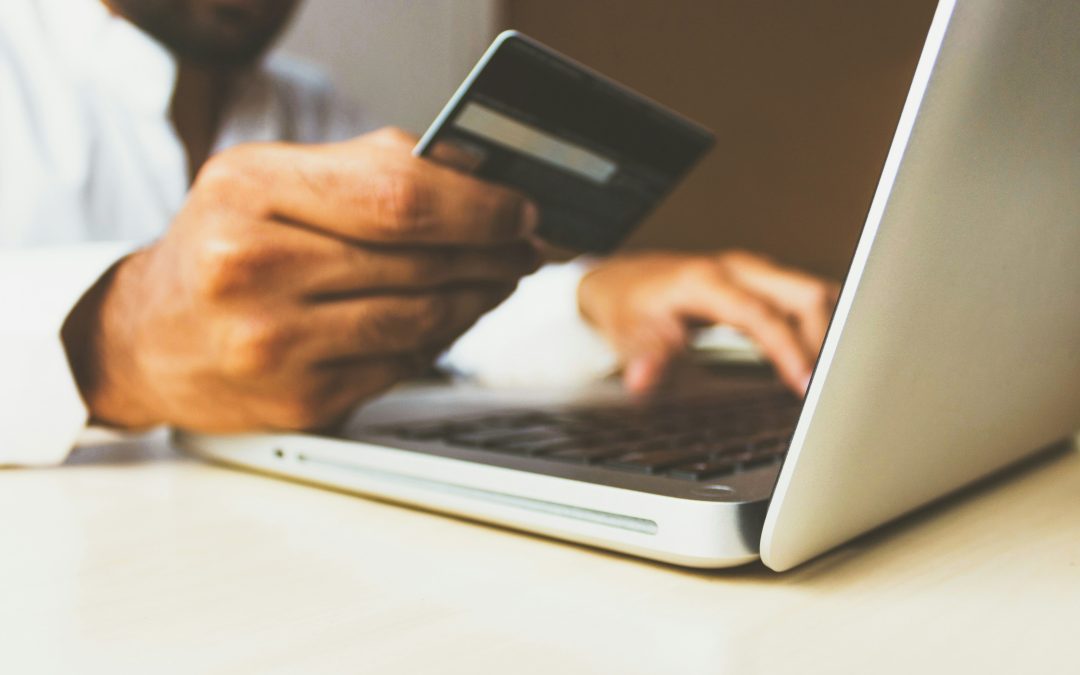 A person is holding a credit card and using a laptop, likely making an online purchase.