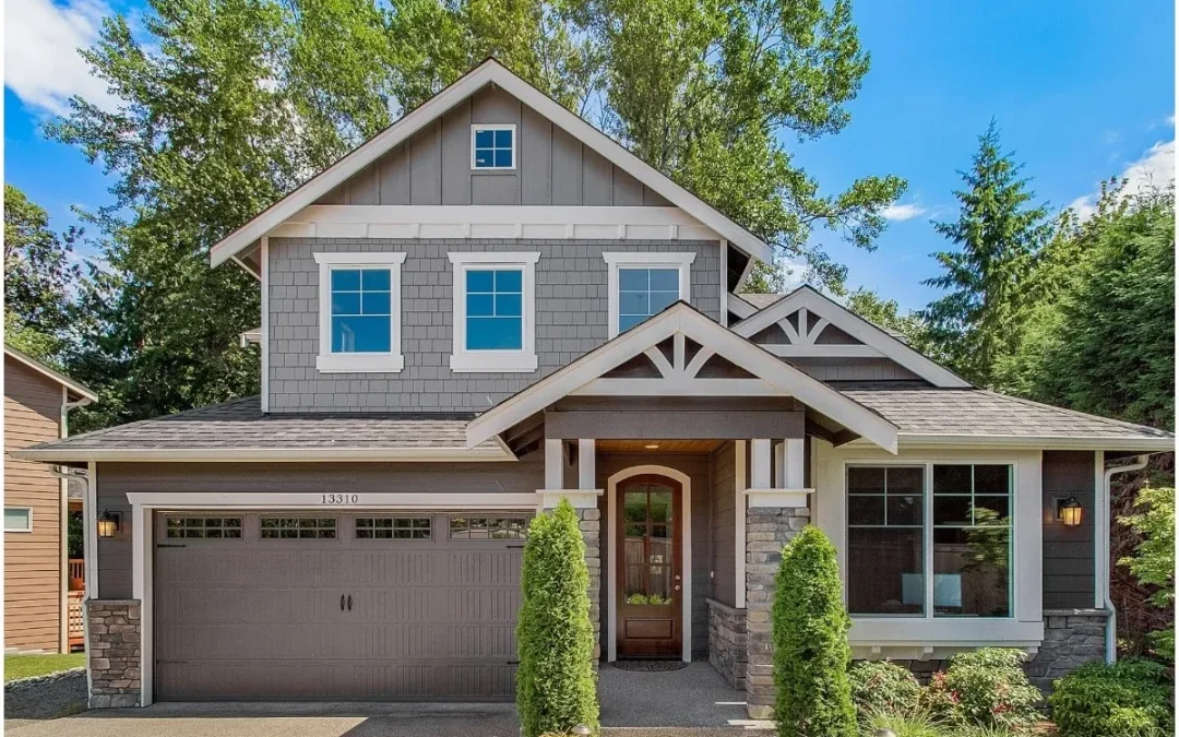 A two-story house with a garage, stone accents, and greenery under a blue sky.