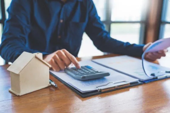 Calculating finances at a desk with a model house, implying real estate planning.
