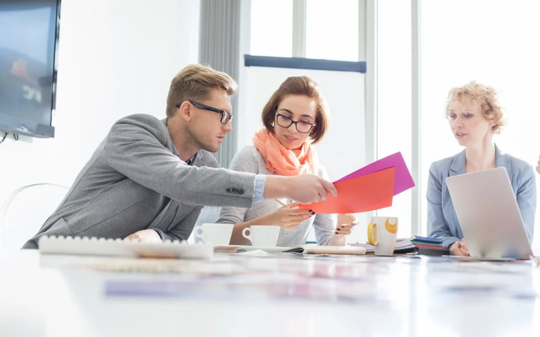 Three professionals examine documents at a bright office meeting table.